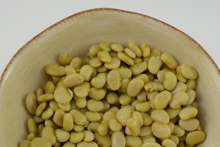 Oregano & Garlic Butter Beans Top view of lima beans in cream colored rustic bowl with a white background.